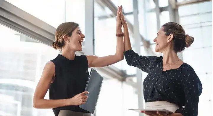 Imagen de dos mujeres de negocios chocan los cinco, felices y exitosas.